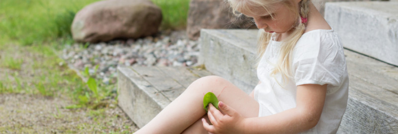 Picture of little girl covering her wounds with a green leaf in her leg.