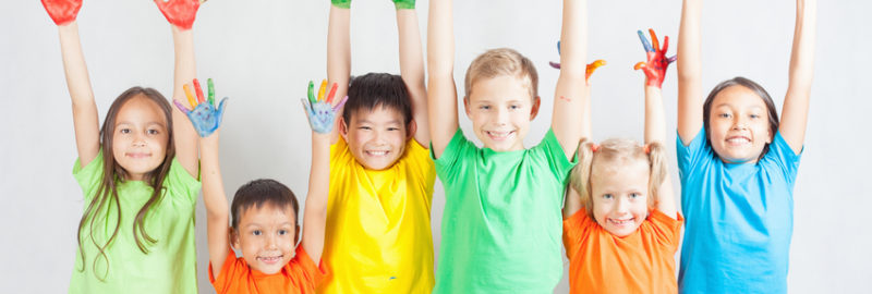 Six happy children wearing multiple colors raising their arms with their hands painted