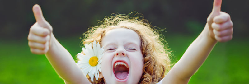 Photo of a beautiful young girl with a flower on her ear while raising her two thumbs.