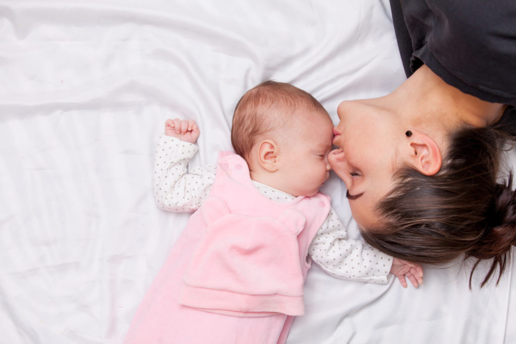 Mother kissing the forehead of her little baby in the bed.