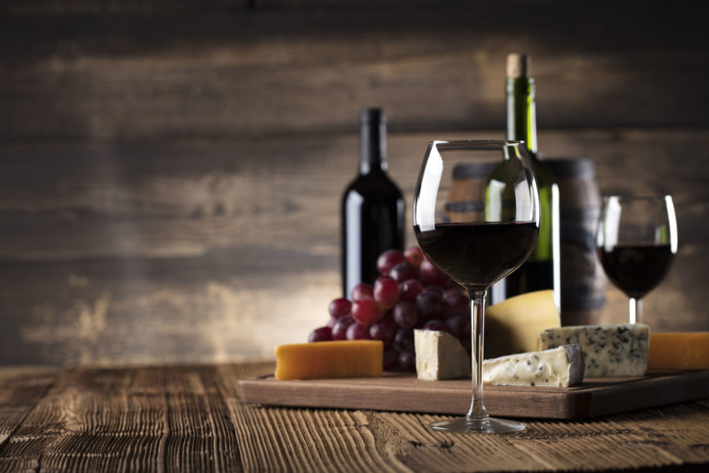 Red wine with cheese and grapes with a rustic background
