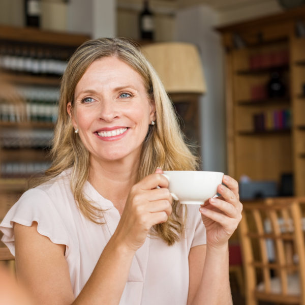 Smiling mature woman holding coffee cup and talking with her friend.