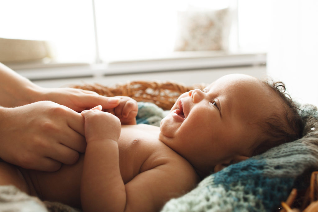 Adorable newborn child smiling and looking up at mother and holding her hands