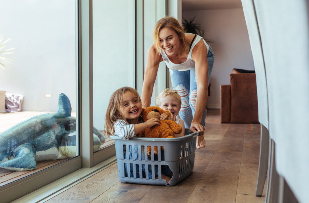 Happy young mother pushing her 2 children sitting in laundry basket at home